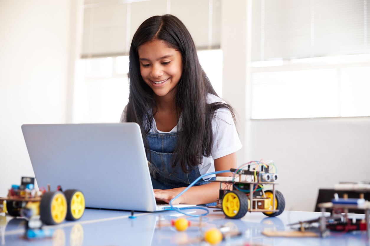 Female student sitting at a computer building and programming robot vehicle