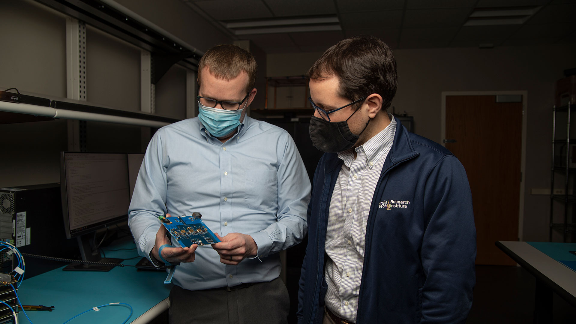 Two researchers in lab examine circuit board.