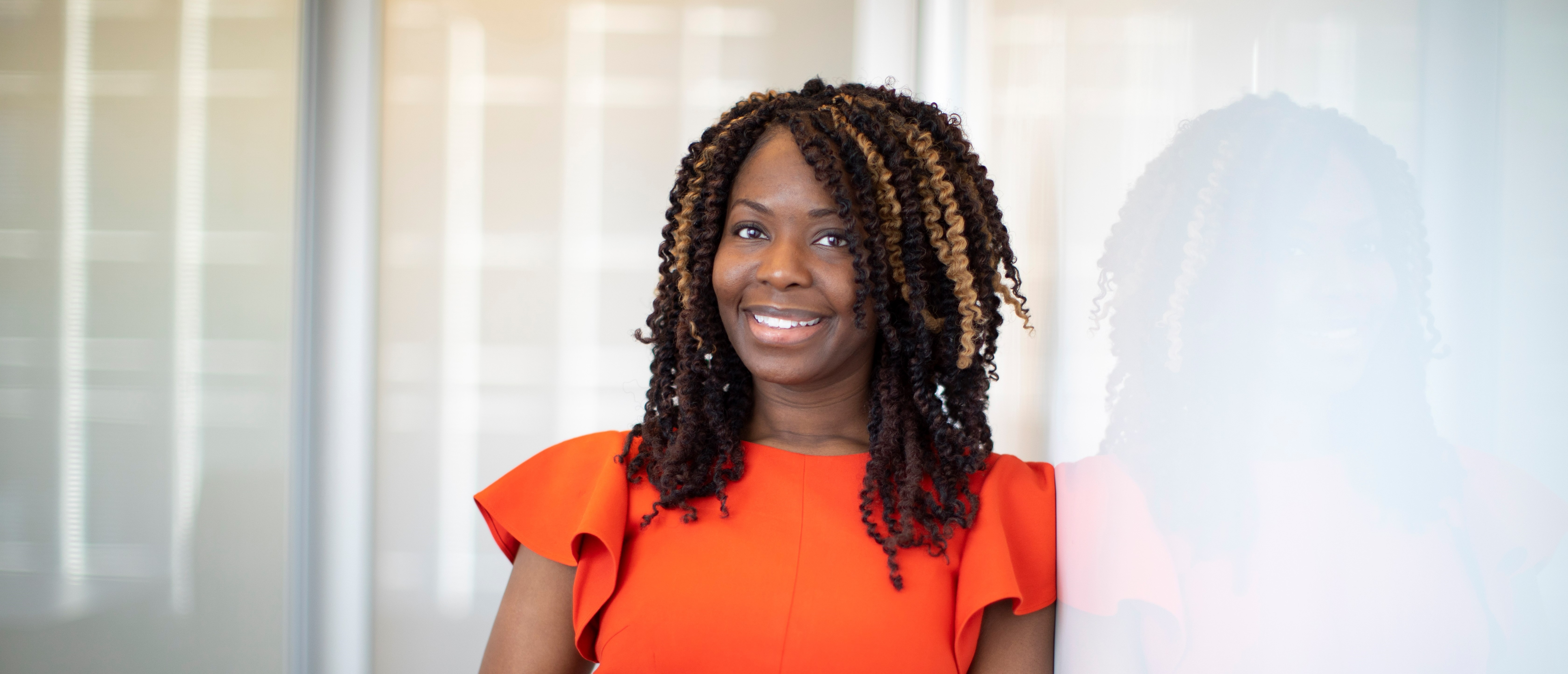 Insider Threat Program Analyst Chikita Sanders stands next to a white board in an orange dress.