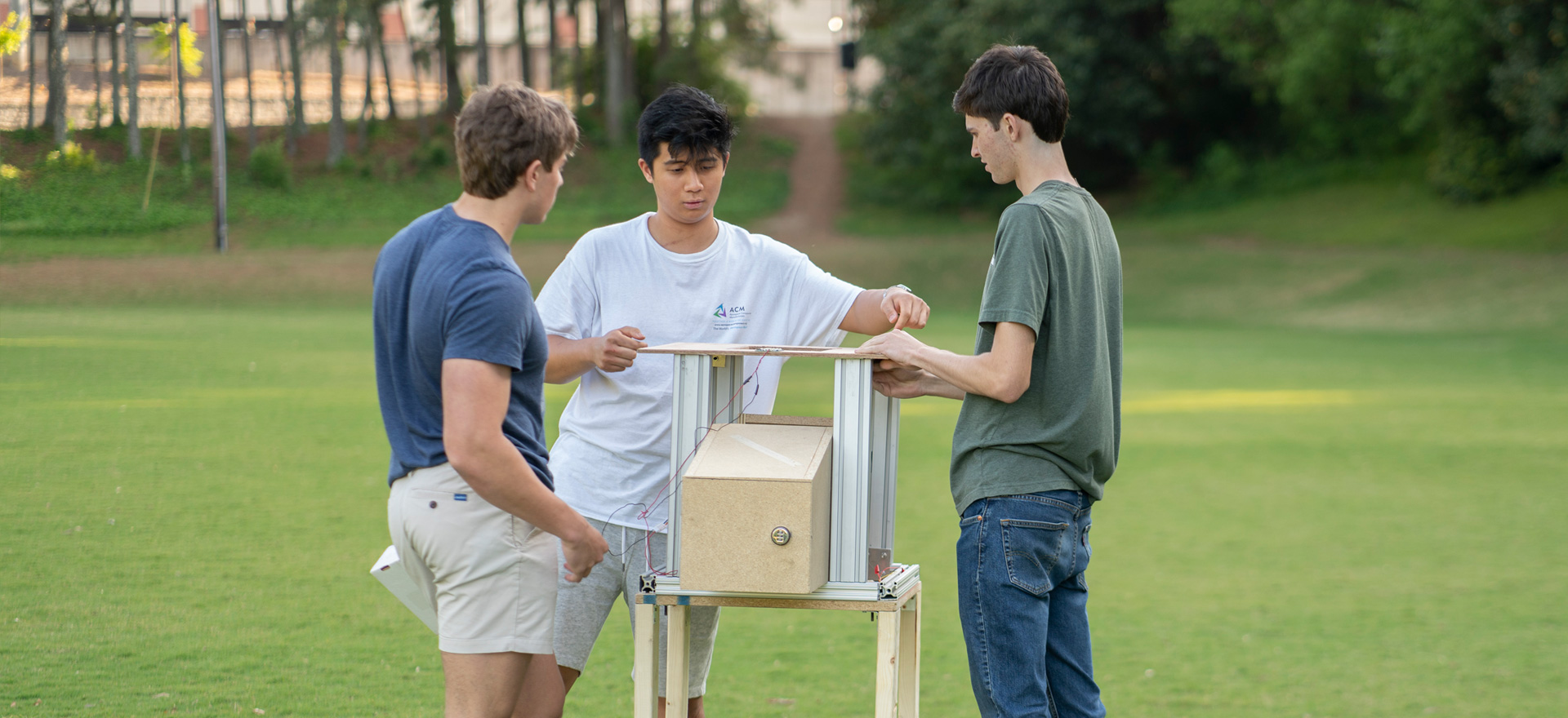 Three male students standing around a mock-up of a package locker made from plywood and metal.