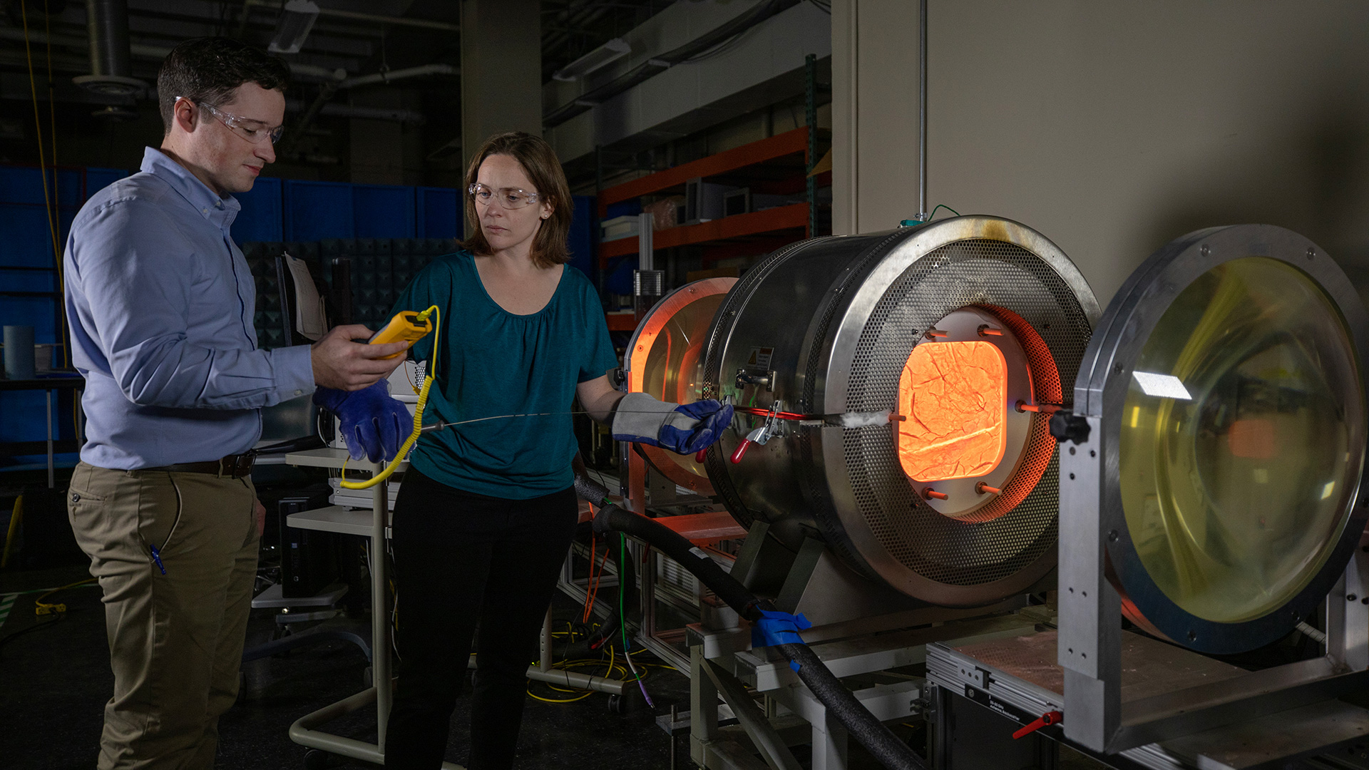 Two research standing in front of large furnace device glowing red.