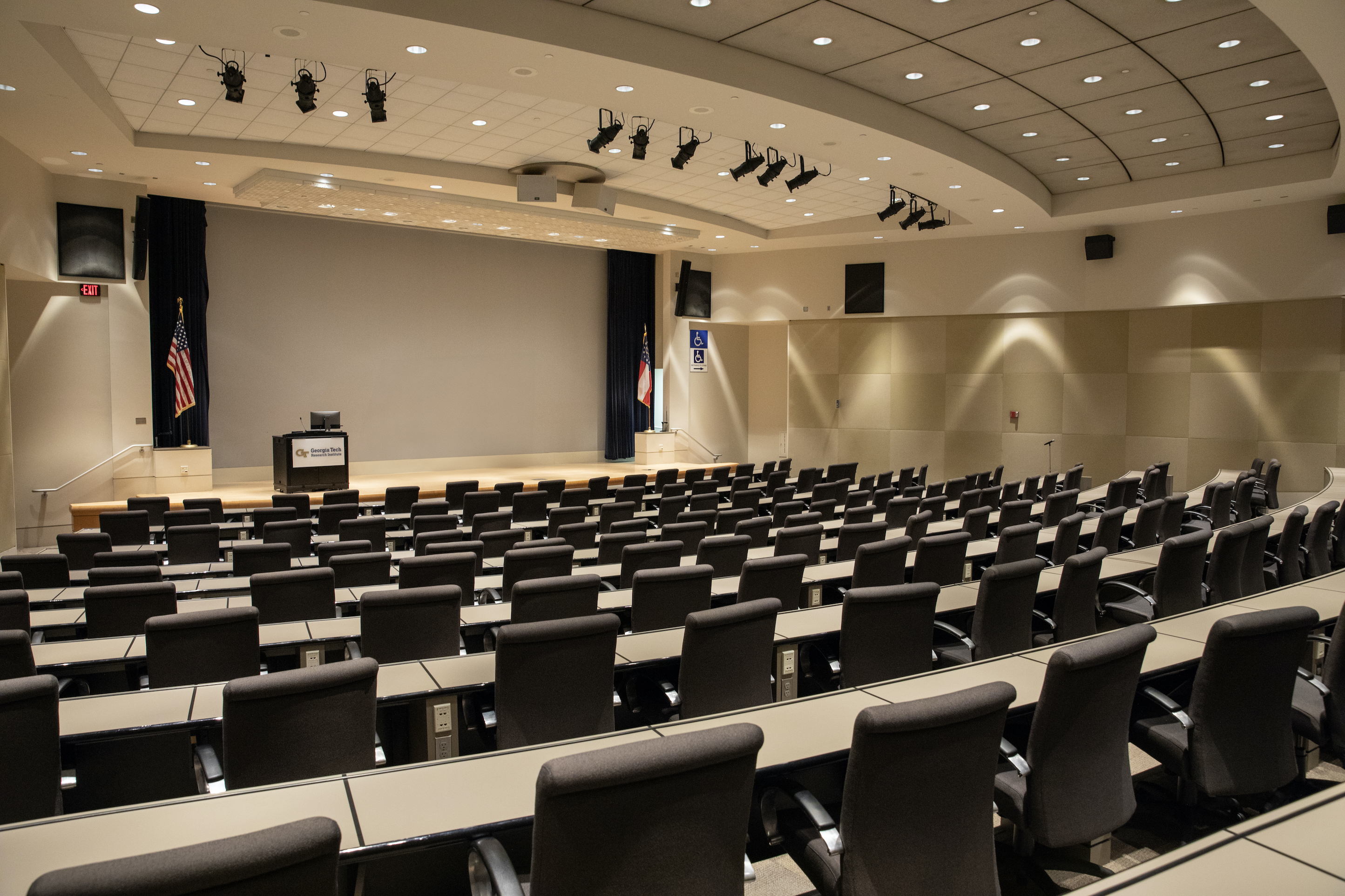 Empty auditorium with many chairs and desks facing a screen and a lectern
