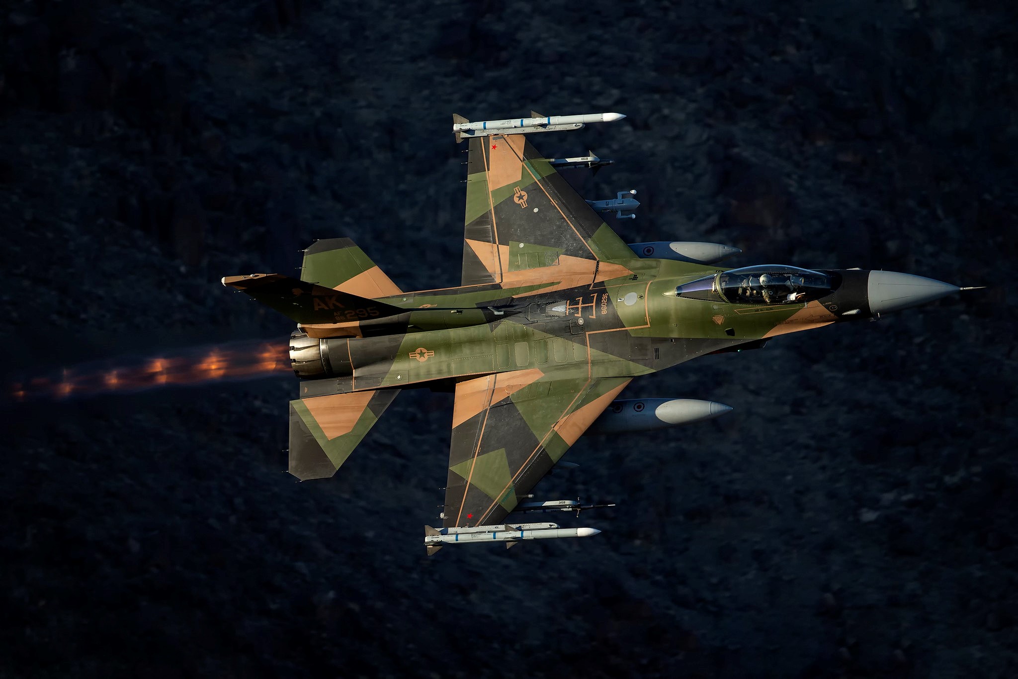 f-16 figher jet with camoflouge paint flying in a dark sky