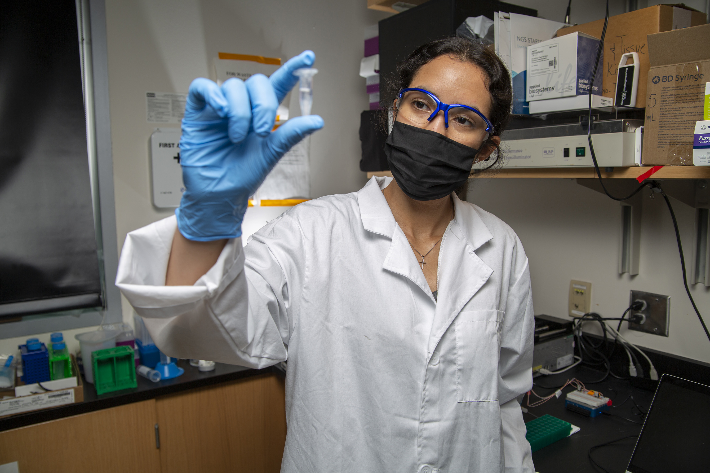 Researcher with a white jacket holding up a small test tube inside a laboratory