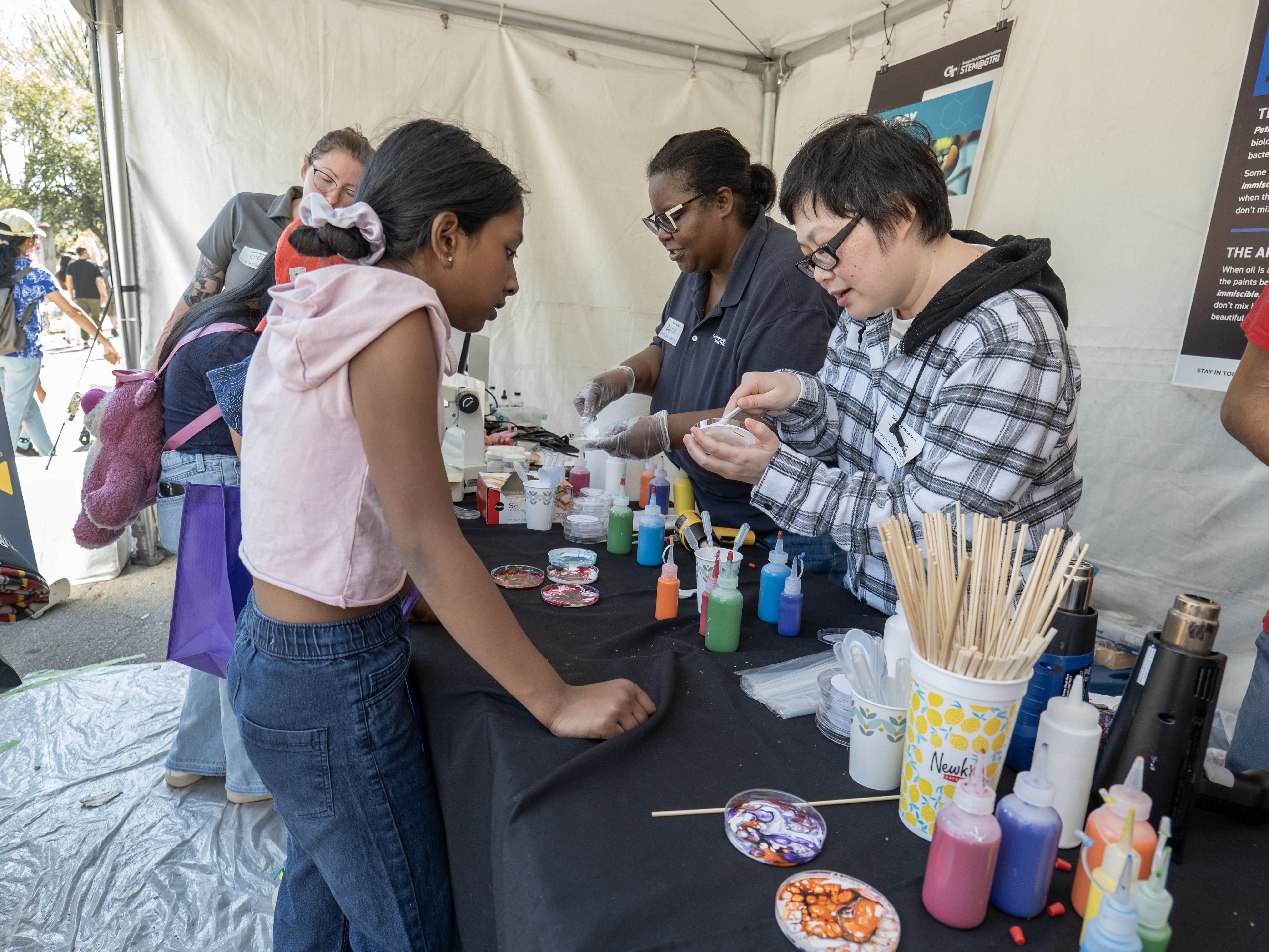 People gathered around a table under a tent doing arts and crafts with paint and supplies.