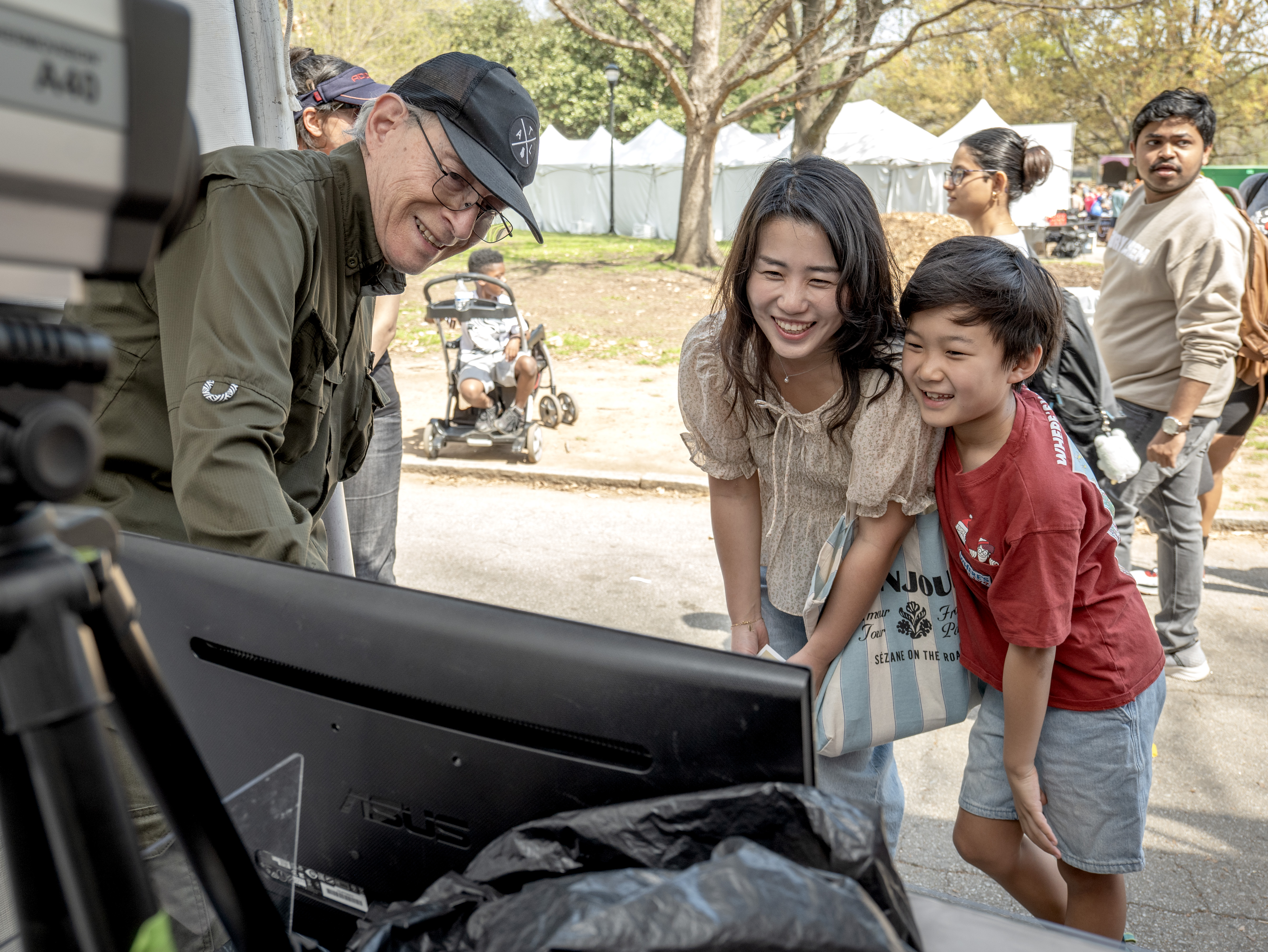 3 individuals looking at a computer screen with other people walking by in the background.
