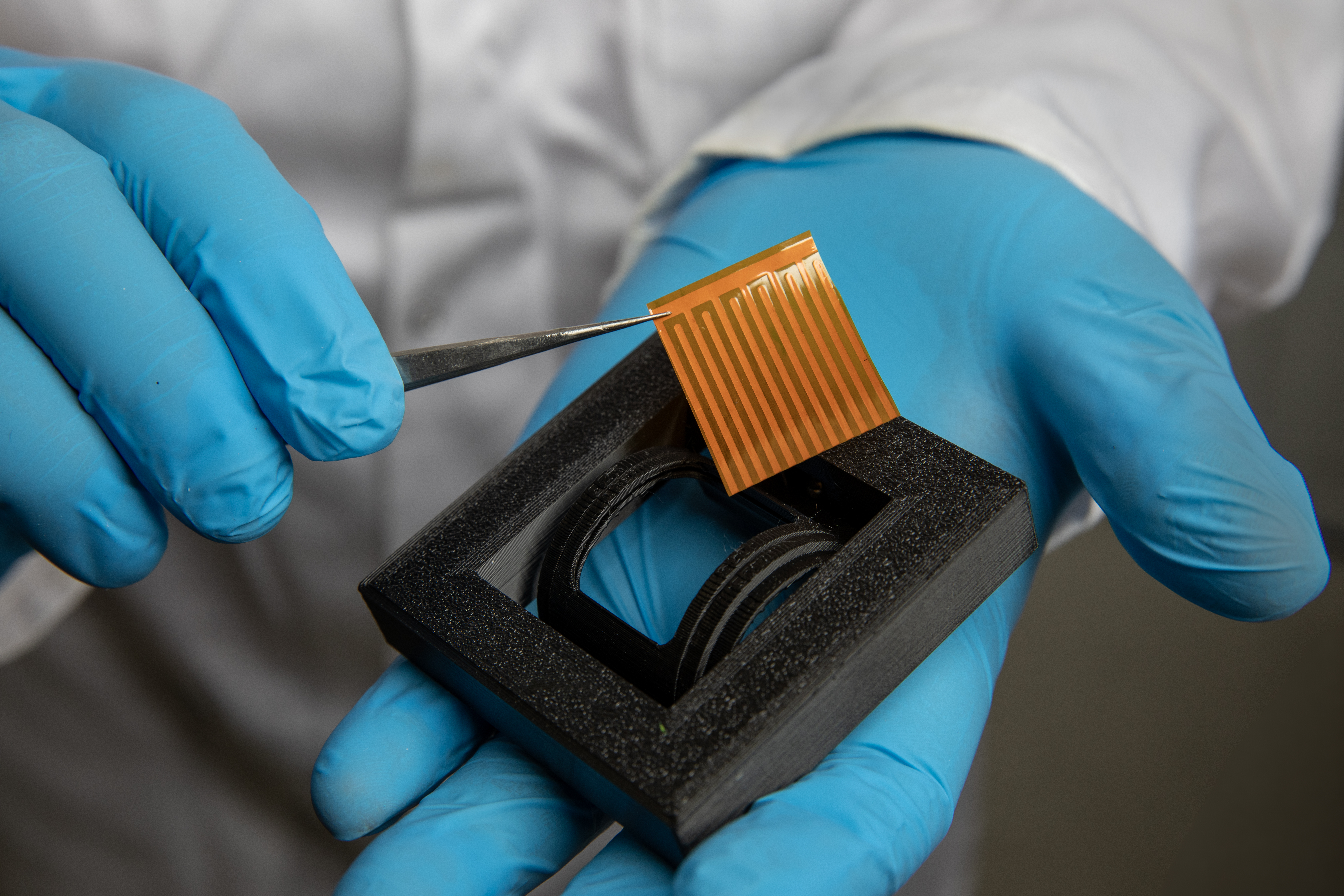 Gloved hands hold orange lightweight material sample and black foam housing developed by GTRI for ISS Materials Experiment 22 testing.
