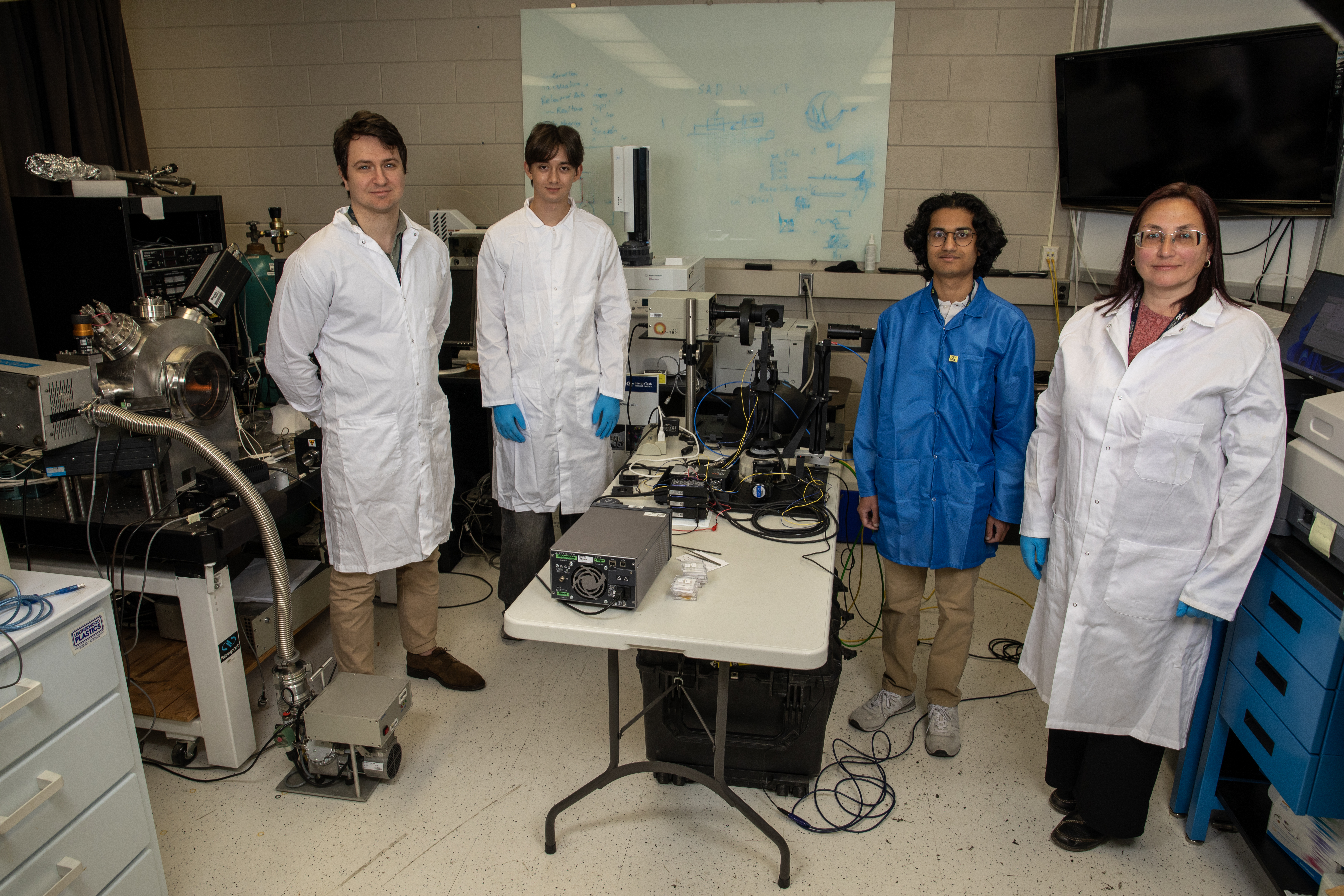 Four GTRI researchers in lab coats stand in laboratory with scientific equipment used to develop materials for ISS Experiment 22.