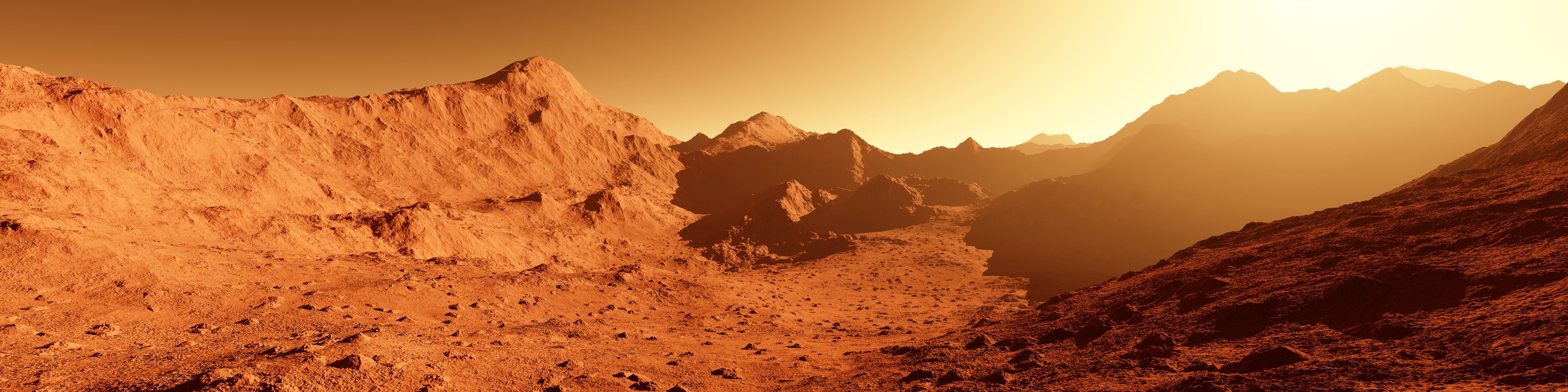Rocky desert landscape with mountain ridges under a golden-orange hazy sky, resembling Mars or an arid alien terrain at sunset.