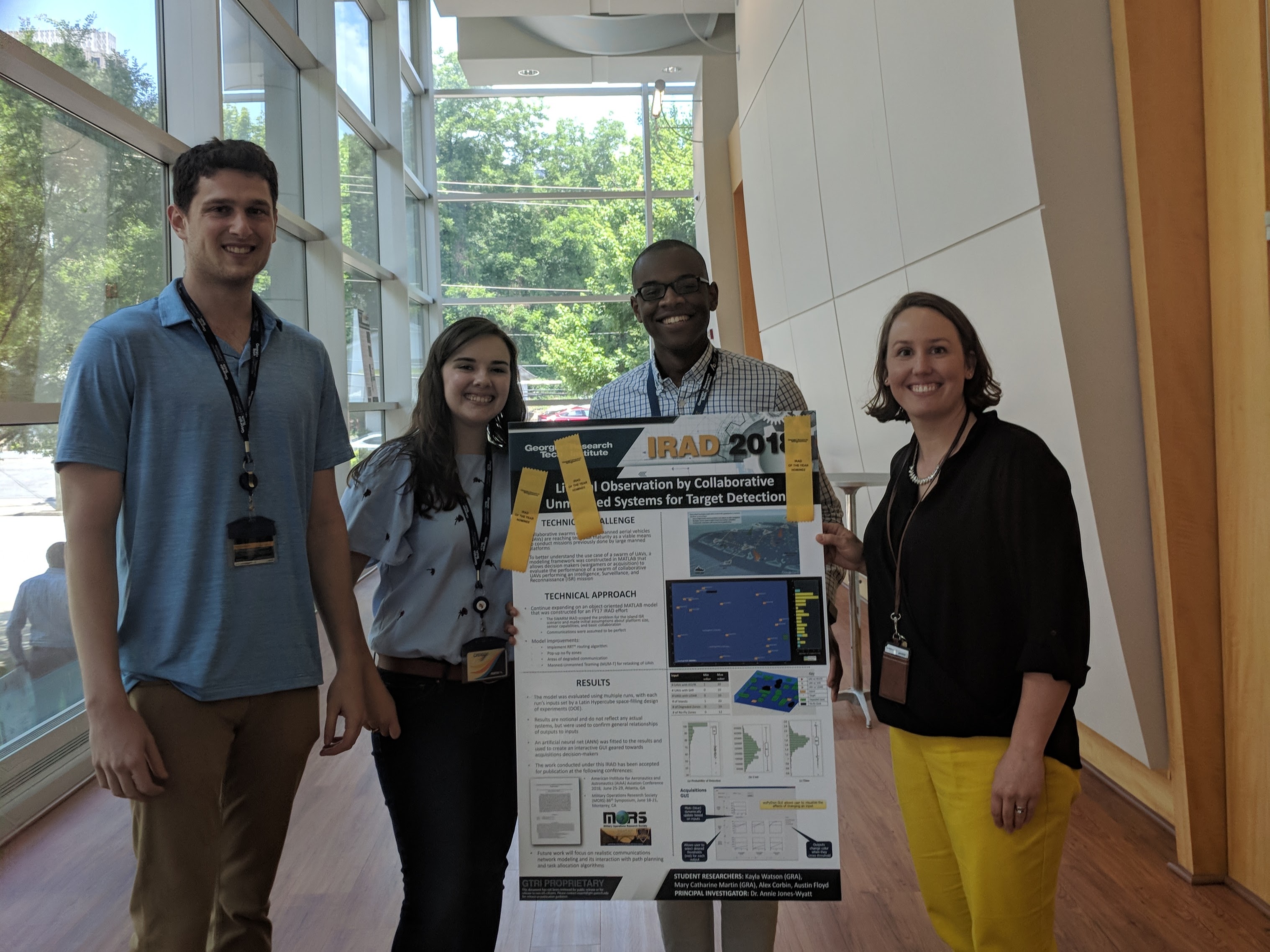 Mary Catharine Martin presents a project poster at a GTRI event, standing with her supervisor, Annie Jones-Wyatt (far right), former GTRI graduate research assistant Troy Sandler (far left), and former GTRI intern Austin Floyd (left of Jones-Wyatt).  Credit: Lynn Fountain