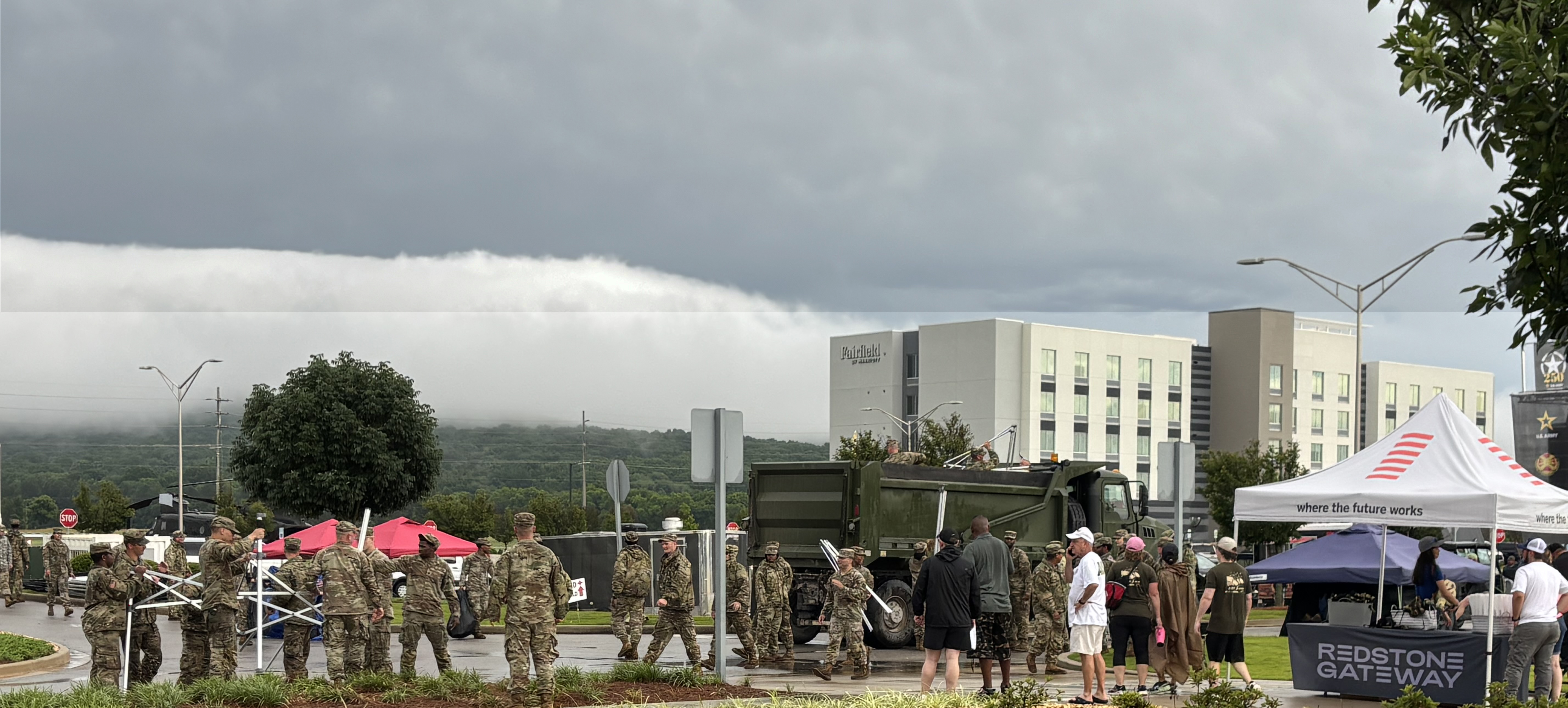 U.S. Army soldiers and others gather under the remnants of dark storm clouds.