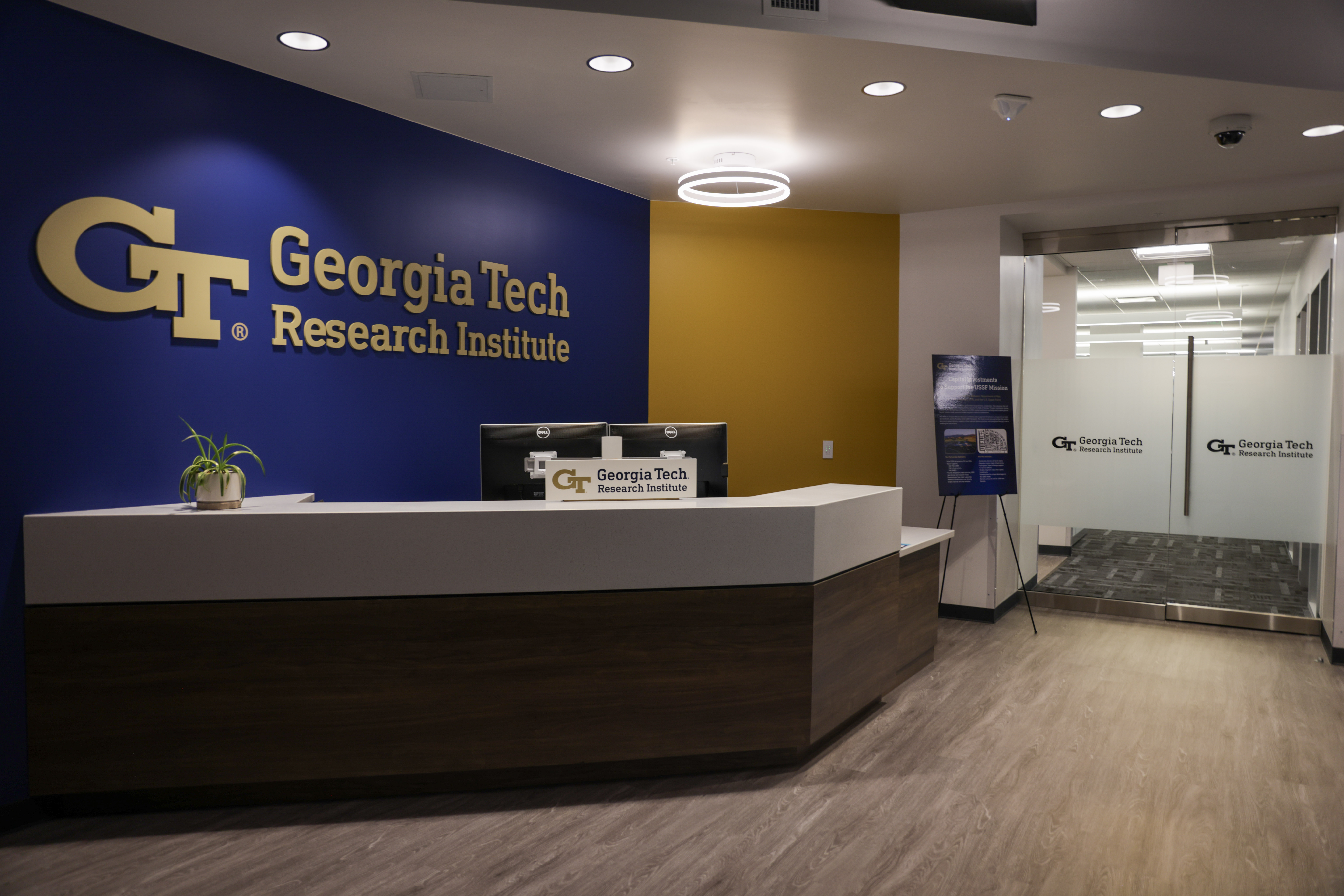 Modern office reception area with Georgia Tech Research Institute logo on navy blue wall, white desk, and glass conference room visible.