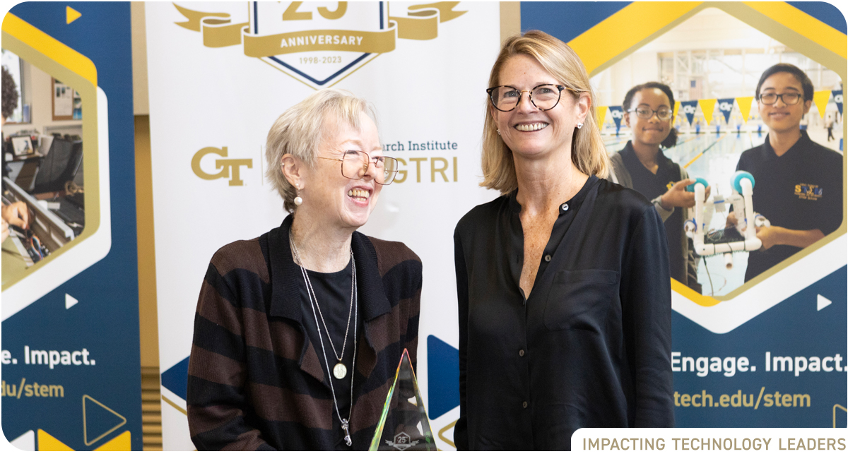 photo: two senior white women standing in front of banner with STEM@GTRI anniversary logos
