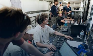 Several researchers with headsets at monitors controlling UAV