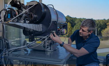 Male researcher examines large round metal Lidar system device.