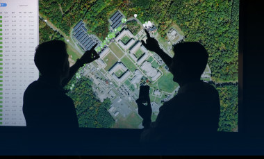Silhouette of two researchers in front of monitors displaying aerial view.