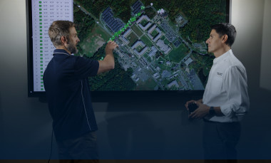 Two male researchers looking and pointing at monitor displaying aerial view of terrain.
