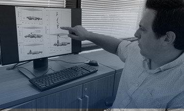 Researcher at desk pointing at computer monitor showing diagrams
