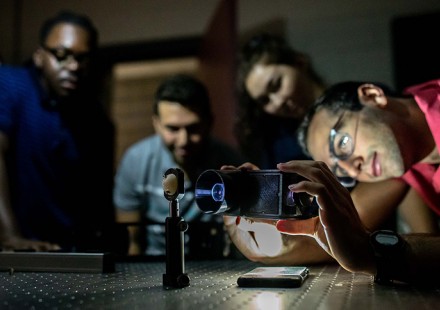 Photo of four interns gathered around a lab table, all appearing to study a device.