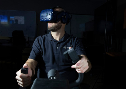 Front view of male researcher wearing VR goggles with hands on flight controls, in a darkened room