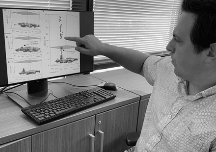 Researcher at desk pointing at computer monitor showing diagrams