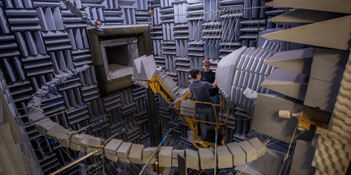 Two researchers in large acoustic research chamber examining test nozzle.
