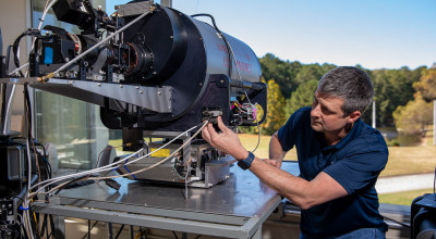 Male researcher examines large round metal Lidar system device.