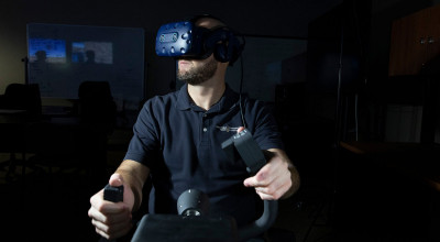Front view of male researcher wearing VR goggles with hands on flight controls, in a darkened room