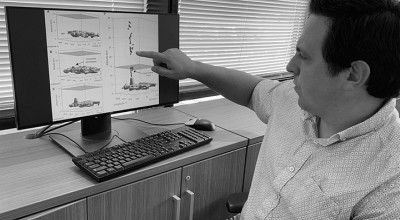 Researcher at desk pointing at computer monitor showing diagrams