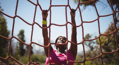 Determined woman climbing a net during obstacle course. Credit iStock.comWavebreakmedia