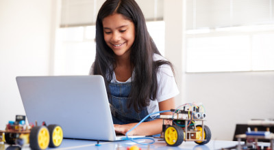 Female student sitting at a computer building and programming robot vehicle