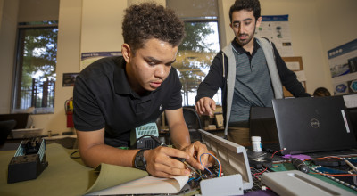 A high school student completing a STEM project with instructor looking over his shoulder. 