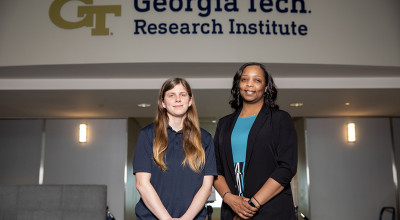 Two women pose in front of the Georgia Tech Research Institute logo in the background. 