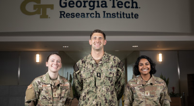 Three members of GTRI's latest Military Graduate Research Program (MGRP) pose in front of GTRI signage.