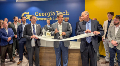 Three men in suits prepare to cut ribbon at Georgia Tech Research Institute office opening ceremony, surrounded by attendees.